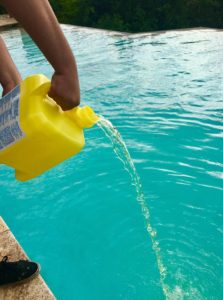 Pool technician adding chlorine shock to a swimming pool at night for optimal water cleanliness.